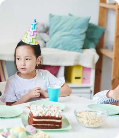 Une petite fille assise à une table avec un gâteau, fourni par un traiteur barbecue